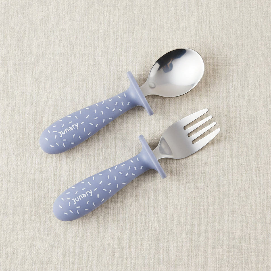 A baby utensil set consisting of a spoon and a fork with blue silicone handles and silver Stainless-steel heads. Speckle pattern.