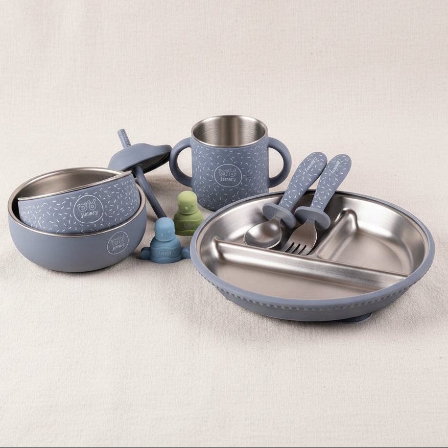 Toddler feeding set with a gripper plate, a sips cup, a little bowl and a mighty bowl, and utensils in a matching blue color with speckled patterns, alongside blue and green pouch toppers.