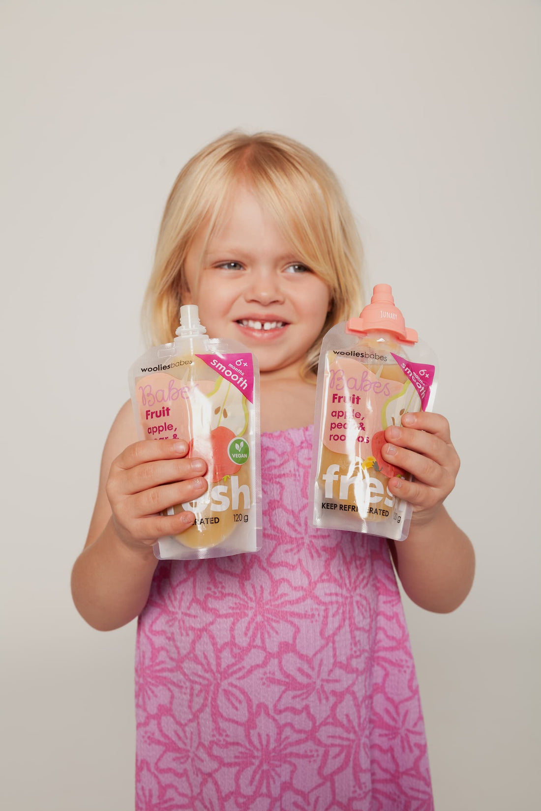 Girl in pink and purple dress holding two food pouches, one with a Junary pink topper on. 