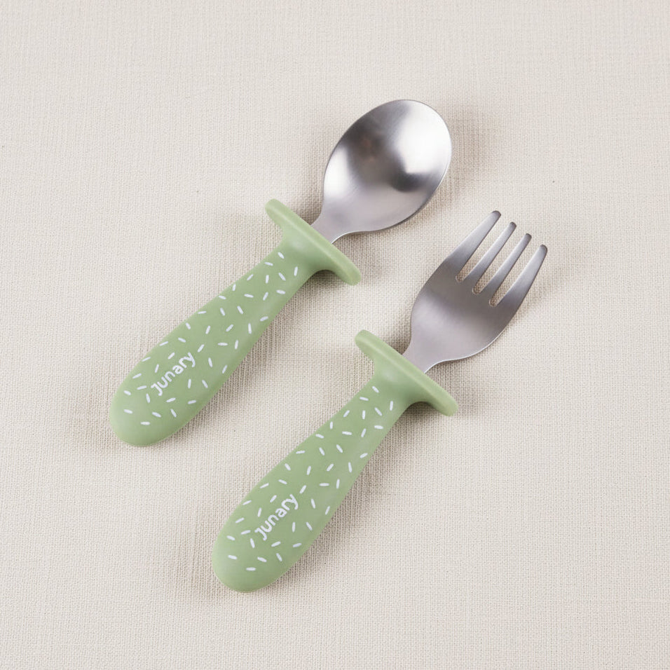 A baby utensil set featuring a spoon and a fork with green speckled pattern handles and silver stainless-steel heads.