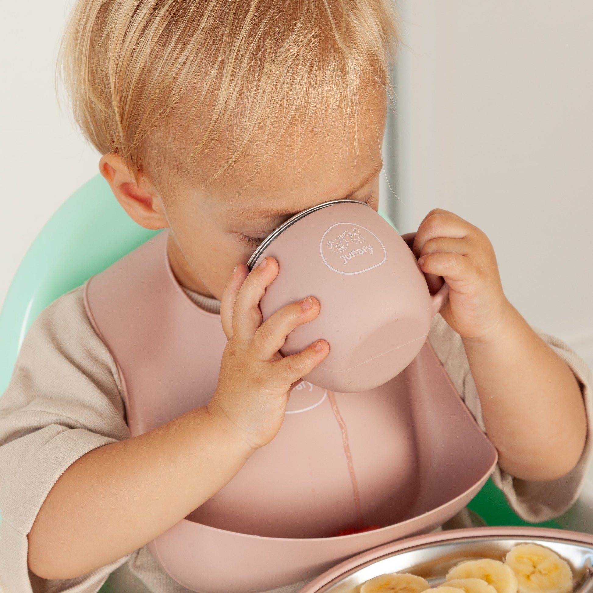 Child in a high chair with a tray of food and a pink cup.