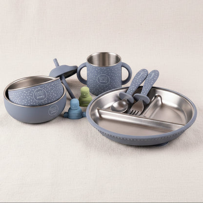 Toddler feeding set with a gripper plate, a sips cup, a little bowl and a mighty bowl, and utensils in a matching blue color with speckled patterns, alongside blue and green pouch toppers.