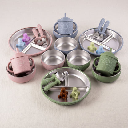 Sets of stainless steel and silicone feeding accessories arranged on a white background, including divided plates, bowls, cups, spoons, forks, blue, and  evergreen.