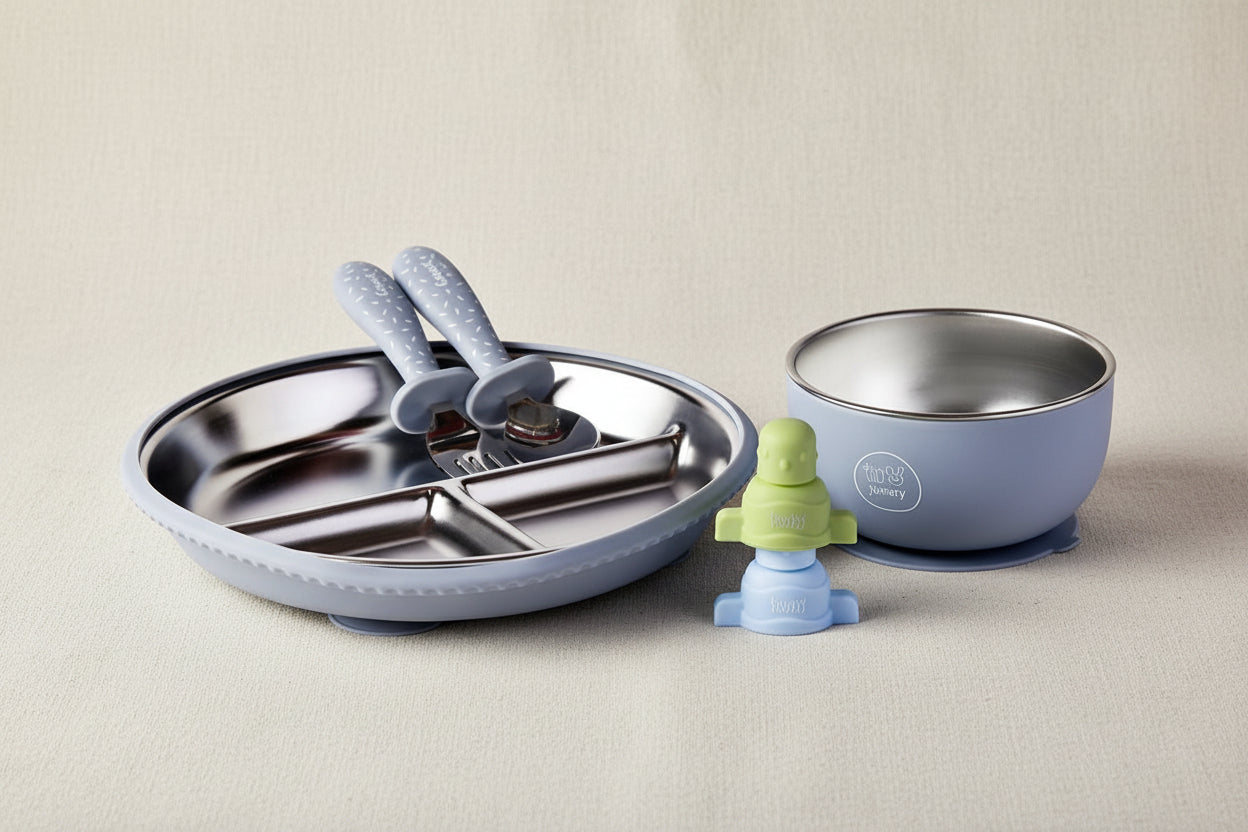 A baby feeding set, including a divided plate with a fork and spoon, a suction blue bowl with a stainless-steel interior, and a small blue and green pouch topper.